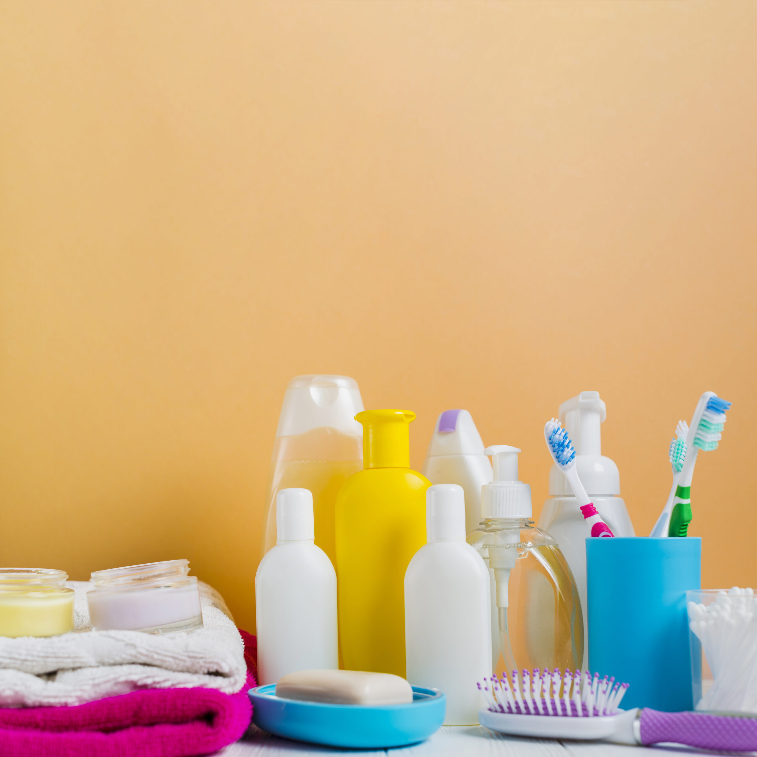 folded-towel-with-cosmetics-products-toothbrushes-against-orange-background Toiletries